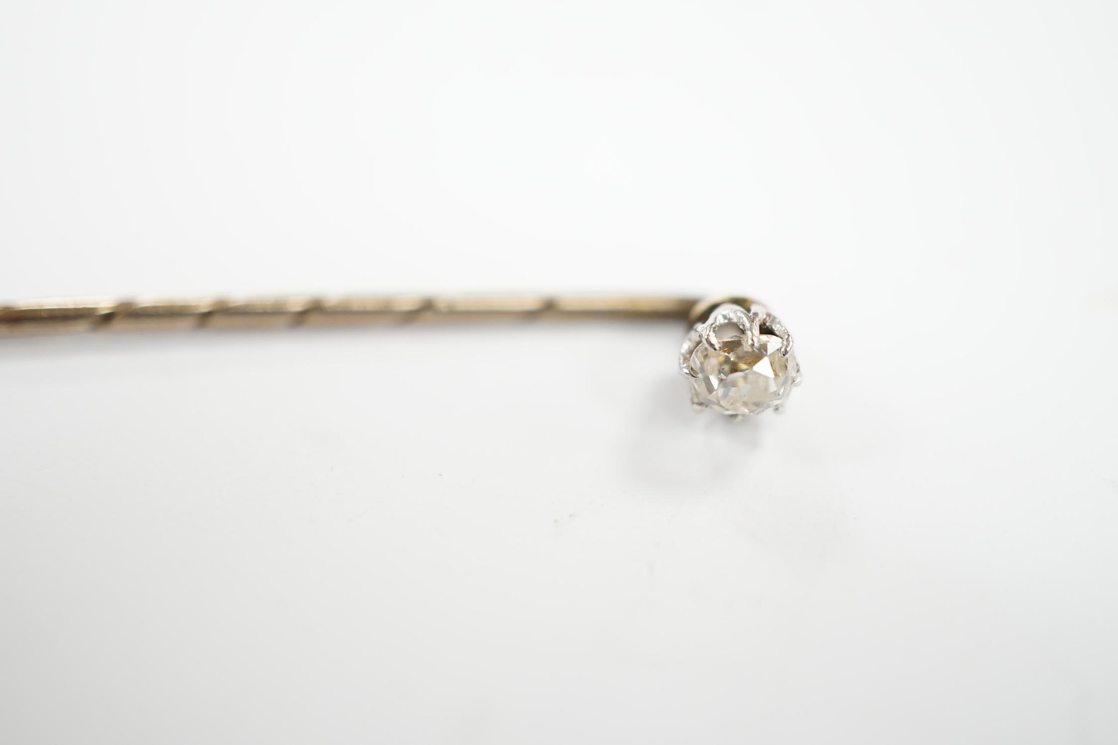 An early 20th century cased yellow metal and cushion cut solitaire diamond set stick pin, 57mm, gross weight 1.3 grams.